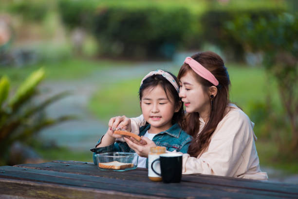 mãe feliz com garotinha fazendo sanduíche em uma mesa de piquenique no parque de outono ensolarado. - little girls autumn child red hair - fotografias e filmes do acervo