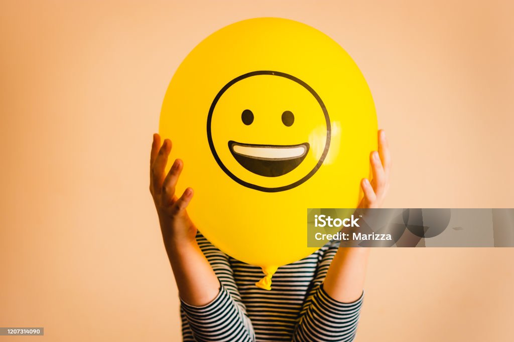 Child holding yellow balloon in the hands Unrecognizable person holding yellow balloon against orange background. Happiness Stock Photo