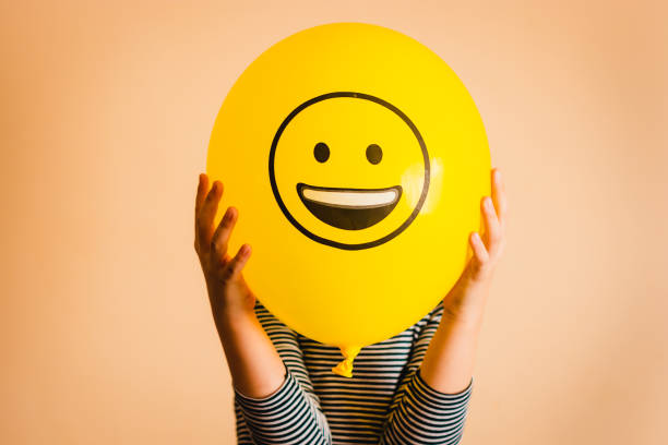 Unrecognizable person holding yellow balloon against orange background.