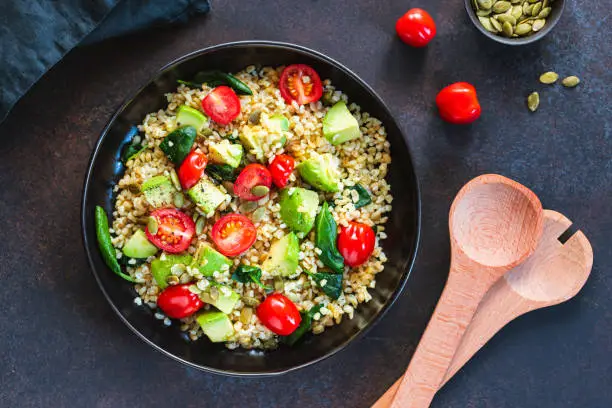 Healthy salad with bulgur, avocado, spinach and cherry tomatoes. Top view.