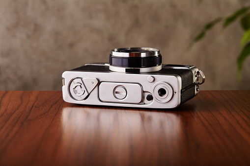 Vintage analog rangefinder film camera on wooden table and concrete textured wall as background