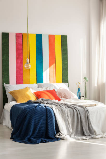 istock Light bulb above cozy bed with pillows and blankets in bright bedroom interior 1207319262
