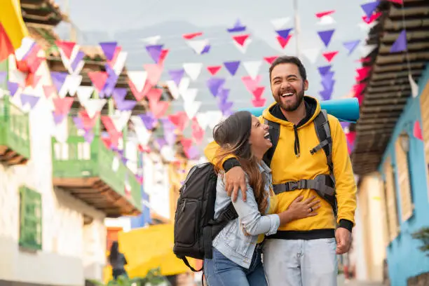Latin couple confused by 25-year-old Latino man dressed casually embraces his partner 25-year-old Latina woman dressed casually shows a beautiful smile as they walk through the colorful streets of Bogota with pennants
