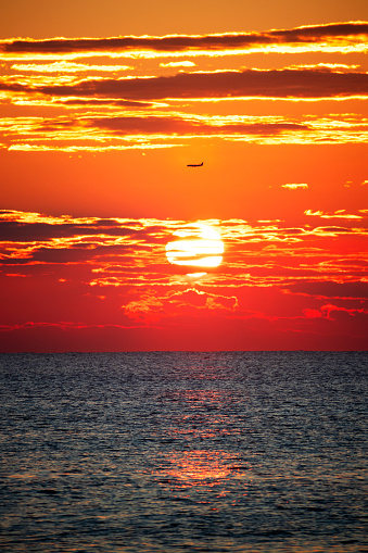 Plane passing by between clouds on sunset, on the beach.