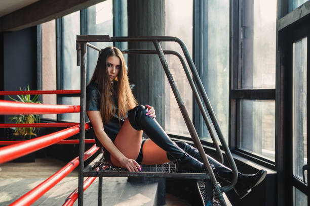 Beautiful attractive young woman wearing leather shorts, jacket and boots posing near boxing ring.