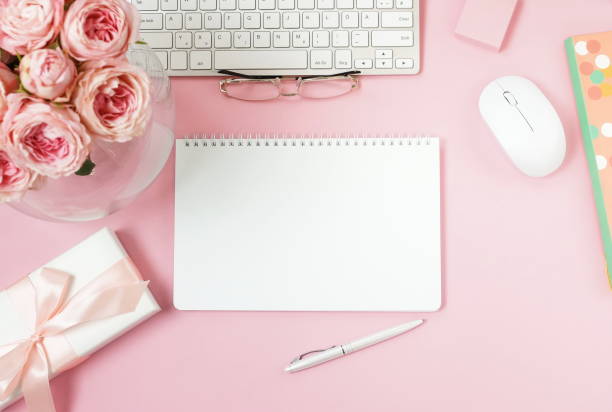 istock flat lay top view women's office desk on  pink background selective focus. Female workspace with laptop, beautiful pink roses flowers in a vase, gift box, accessories, notebook mock up, glasses. 1207326282