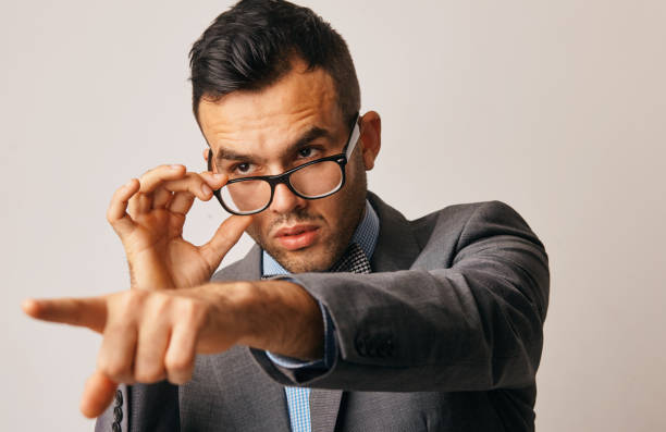 istock a young businessman looks at something from under his glasses and points his finger 1207326613