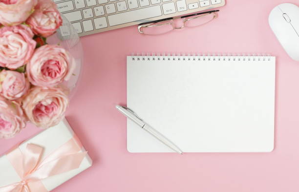 istock flat lay top view women's office desk on  pink background selective focus. Female workspace with laptop, beautiful pink roses flowers in a vase, gift box, accessories, notebook mock up, glasses. 1207327532