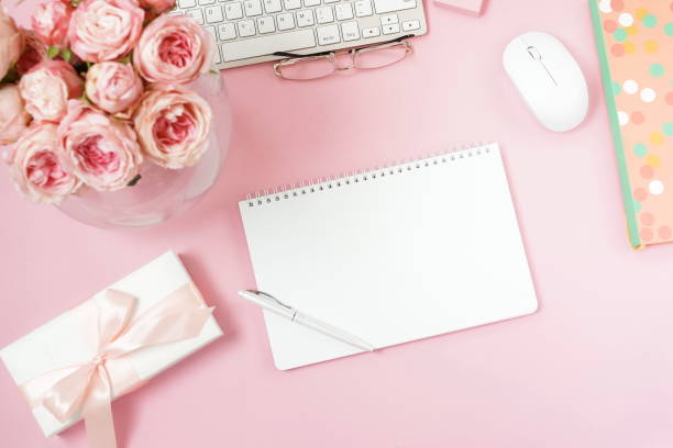istock flat lay top view women's office desk on  pink background selective focus. Female workspace with laptop, beautiful pink roses flowers in a vase, gift box, accessories, notebook mock up, glasses. 1207327569