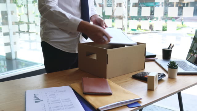4k video of Unhappy employee packing his belongings into cardboard box and leaves office