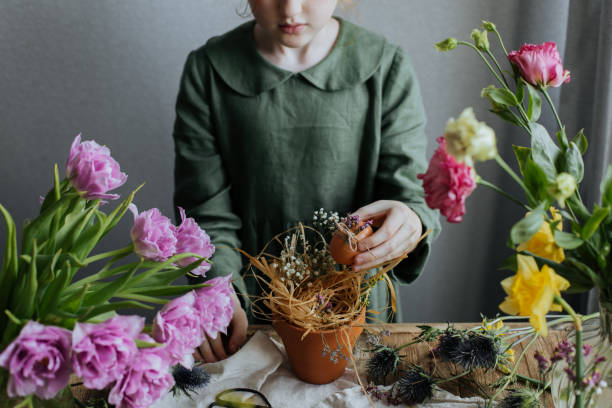 A red-haired little girl in a linen green dress is preparing an Easter decor in a rustic style.