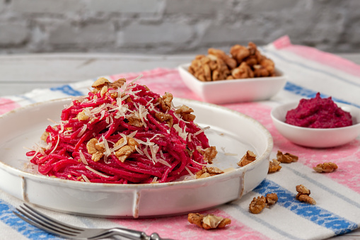 On a light background spaghetti with beetroot pesto sauce, walnuts and parmesan