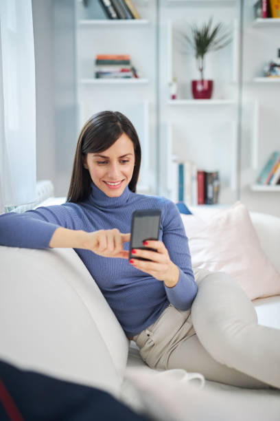 istock Young charming brunette sitting on couch in her beautiful home and typing message. 1207340048