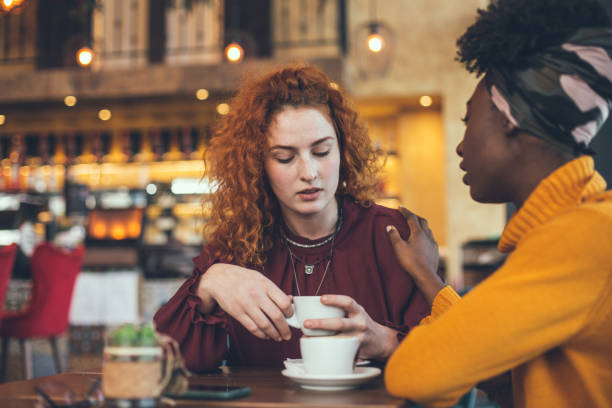 A young woman is talking with a female friend about her problem in a cafe. The friend is supportive and understanding. stock photo