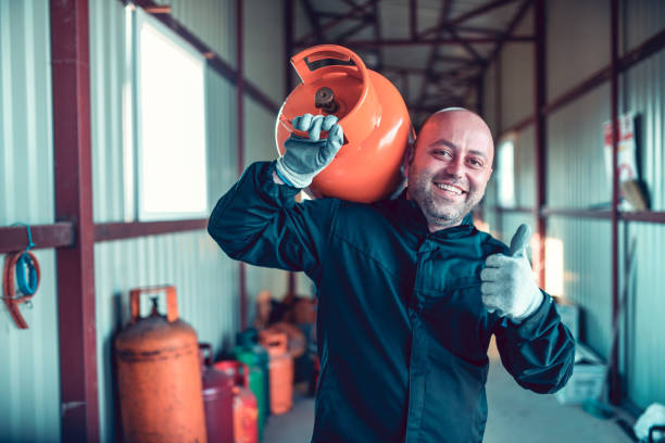 happy liquified gas storage worker carrying gas cylinder on shoulder - liquified petroleum gas imagens e fotografias de stock