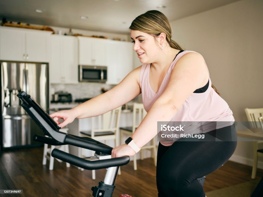 Mujer usando la bicicleta de ejercicio en un hogar - Foto de stock de Andar en bicicleta libre de derechos