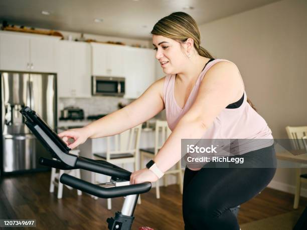Mujer Usando La Bicicleta De Ejercicio En Un Hogar Foto de stock y más banco de imágenes de Andar en bicicleta - Andar en bicicleta, Ejercicio físico, Positividad hacia el cuerpo