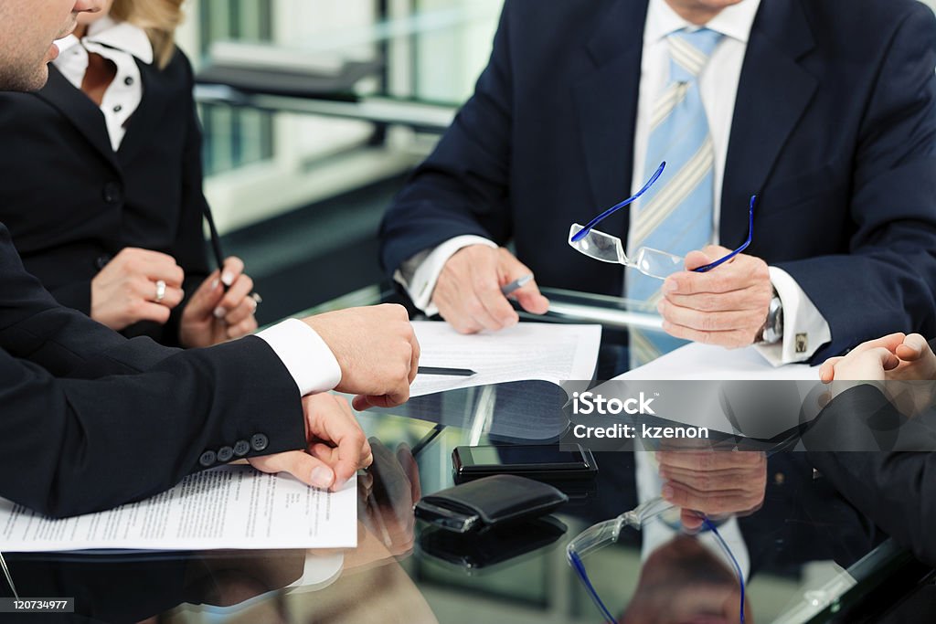 People in business suits with paperwork at desk Business - meeting in an office; lawyers or attorneys discussing a document or contract agreement Law Stock Photo