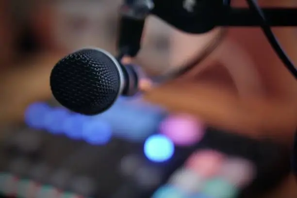Dynamic microphone in the foreground of a radio or podcasting studio with lights from a mixing console. Lovely round bokeh of colorful lights in the background