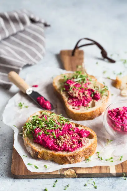 Bruschetta with Beetroot hummus decorated with chopped nuts and microgreen. Vegan recipes, plant-based dishes. Green living concept. Organic food. Vegetarian cuisine. Bread with pink dipping sauce