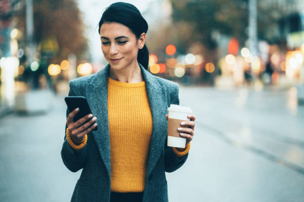 Texting in the city Modern young woman walking on the city street texting and holding cup of coffee scrolling photos stock pictures, royalty-free photos & images