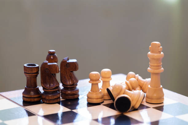 istock Chess pieces on a chessboard. A group of black chess pieces attack the white king. The White King is protected by pawns. 1207355357