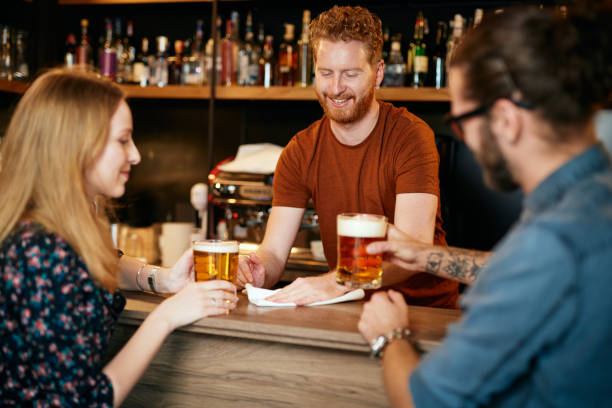 笑顔のバーメンは、顧客にサービスを提供し、バーカウンターを拭きます。 - drinking couple bar counter bar ストックフォトと画像