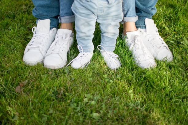 happy family concept. the legs of a father, mother and child in white sneakers on a grass - healthy lifestyle nature sports shoe childhood imagens e fotografias de stock