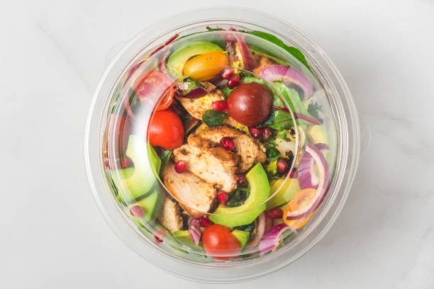 Plastic package with healthy chicken salad with avocado , tomatoes and pomegranate to take away