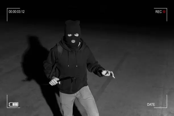 Surveillance camera caught burglar in ski mask holding crowbar while making eye contact in dark parking lot
