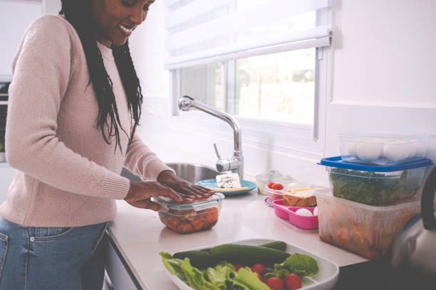 A woman keeping leftovers. A young woman packing leftovers into a plastic container, cooking at a domestic kitchen. leftovers photos stock pictures, royalty-free photos & images