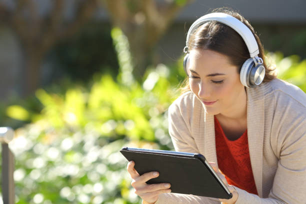 mujer con auriculares viendo los medios en la tableta en un parque - sun watch fotografías e imágenes de stock