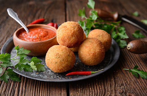 Homemade classic Arancini Di Riso, crispy Sicilian rice balls stuffed with Mozzarella cheese, served with hot Arrabbiata dipping sauce on rustic wooden background