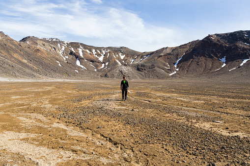 One man with a hat, standing in middle of desertic landscape in Tongariro National Park, Waikato, New Zealand