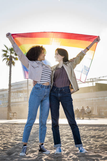 dwie gejowskie dziewczyny wymachujące tęczową flagą - multi ethnic group couple sex women zdjęcia i obrazy z banku zdjęć