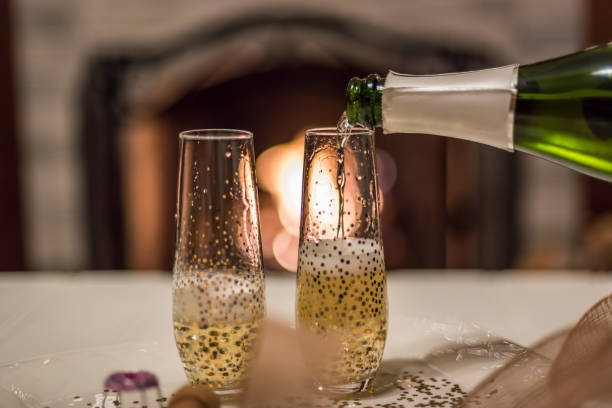 pouring champagne from bottle into glass in front of the fireplace - date night imagens e fotografias de stock