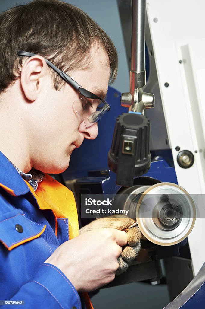worker at machine tool operating worker in uniform and protective glasses working on sharpening machine tool Accuracy Stock Photo