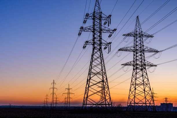 high voltage power line in a field at sunset - torre de alta imagens e fotografias de stock