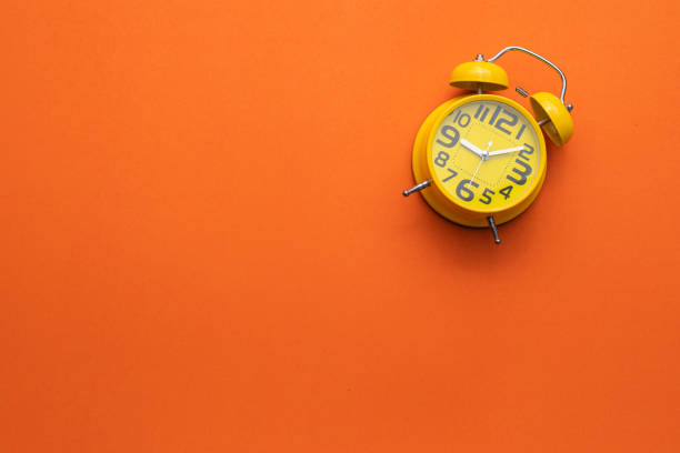 istock Yellow alarm clock on the middle of orange background 1207413600