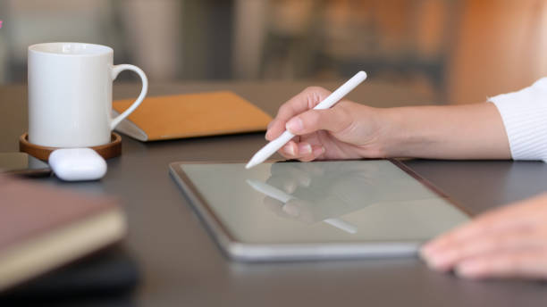 istock Close up view of college girl writing on mock up tablet while working on her project on wooden desk 1207433018