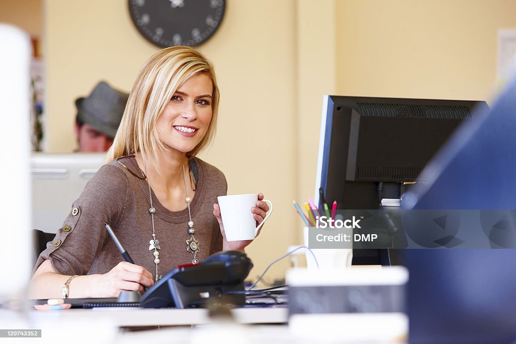 Portrait of a Beautiful Young Office Worker Young woman works at her desk on a digital tablet while holding a cup of coffee. Horizontal shot. 20-29 Years Stock Photo
