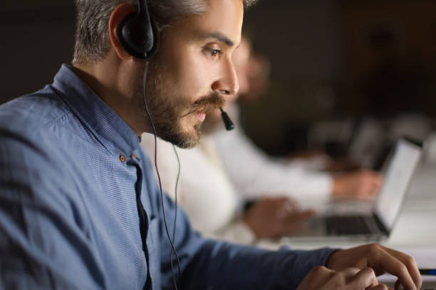 istock Side view of handsome young man with headset looking at laptop 1207435729