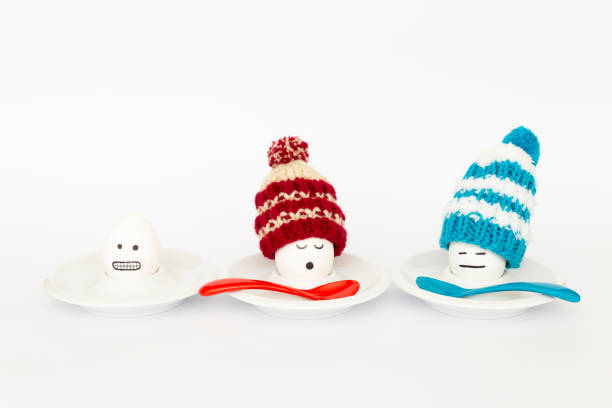Fun breakfast concept with boiled eggs with abstract happy, sleepy and freezing human faces wearing knitted woolen hats on white background