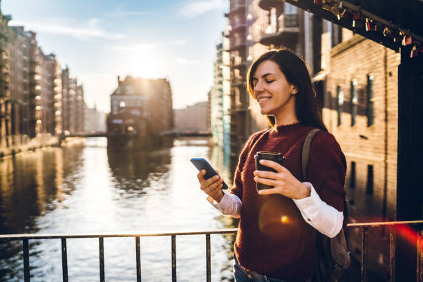 Young tourist woman is using phone and drinking coffee in Speicherstadt, old part of Hamburg, Germany.