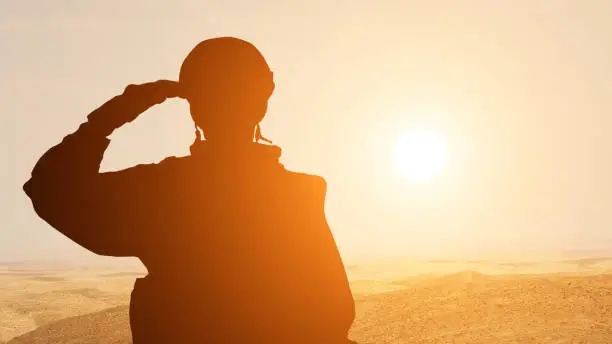 Photo of Silhouette Of A Solider Saluting Against the Sunrise in the desert of the Middle East. Concept - armed forces of UAE, Israel, Egypt