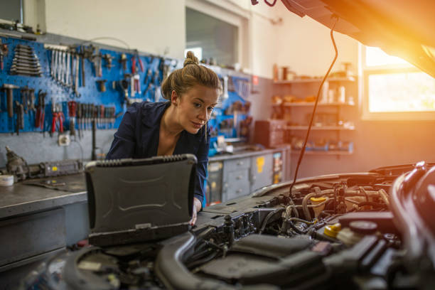 한 여성 정비사가 차고 수리점에서 자동차의 보닛 아래에서 일하고 있습니다. - auto mechanic adult auto repair shop blue 뉴스 사진 이미지