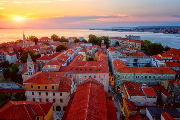 Top view of Zadar old town at sunset from the tower of Zadar cathedral,  Dalmatia, Croatia. Scenic cityscape with historical architecture Top view of Zadar old town at sunset from the tower of Zadar cathedral,  Dalmatia, Croatia. Scenic cityscape with historical architecture, red tiled roofs, sea, sky and sun, outdoor travel background croatian culture photos stock pictures, royalty-free photos & images