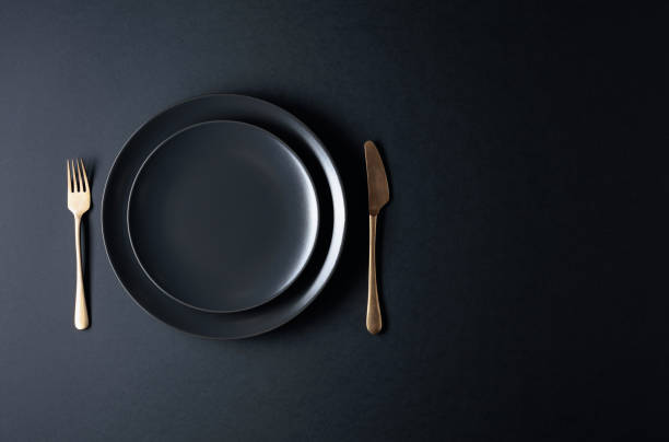 istock Empty black plate, fork and knife on a black background. Top view. 1207460511