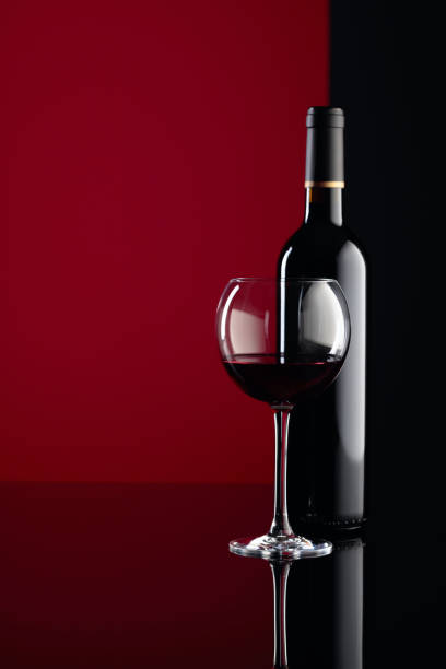 istock Glass and bottle of red wine on a black reflective background. Copy space. 1207462421