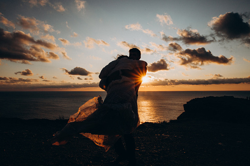 Beautiful couple huggin on cliff edge on sunset. Love and tender.